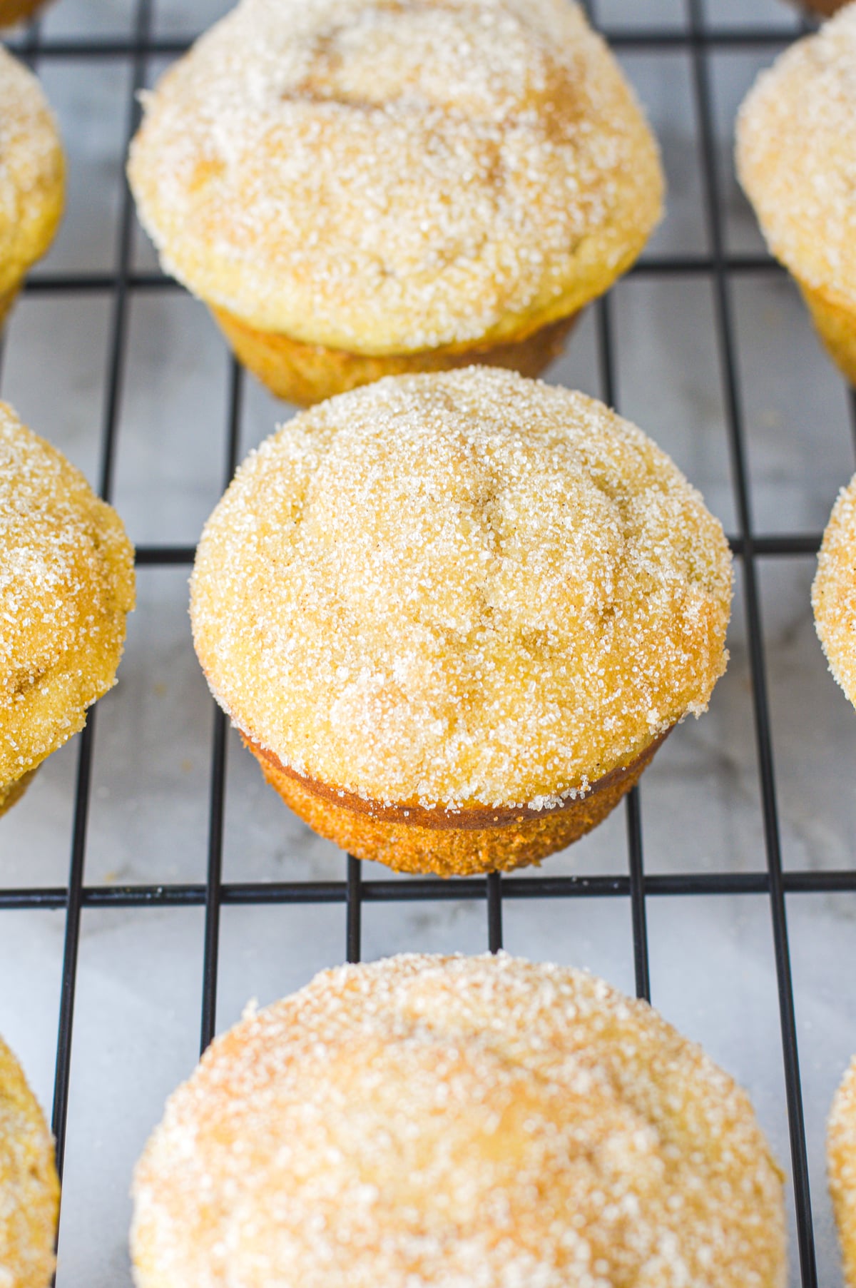 A close-up of homemade donut muffins coated in granulated cinnamon sugar, cooling on a black wire rack.