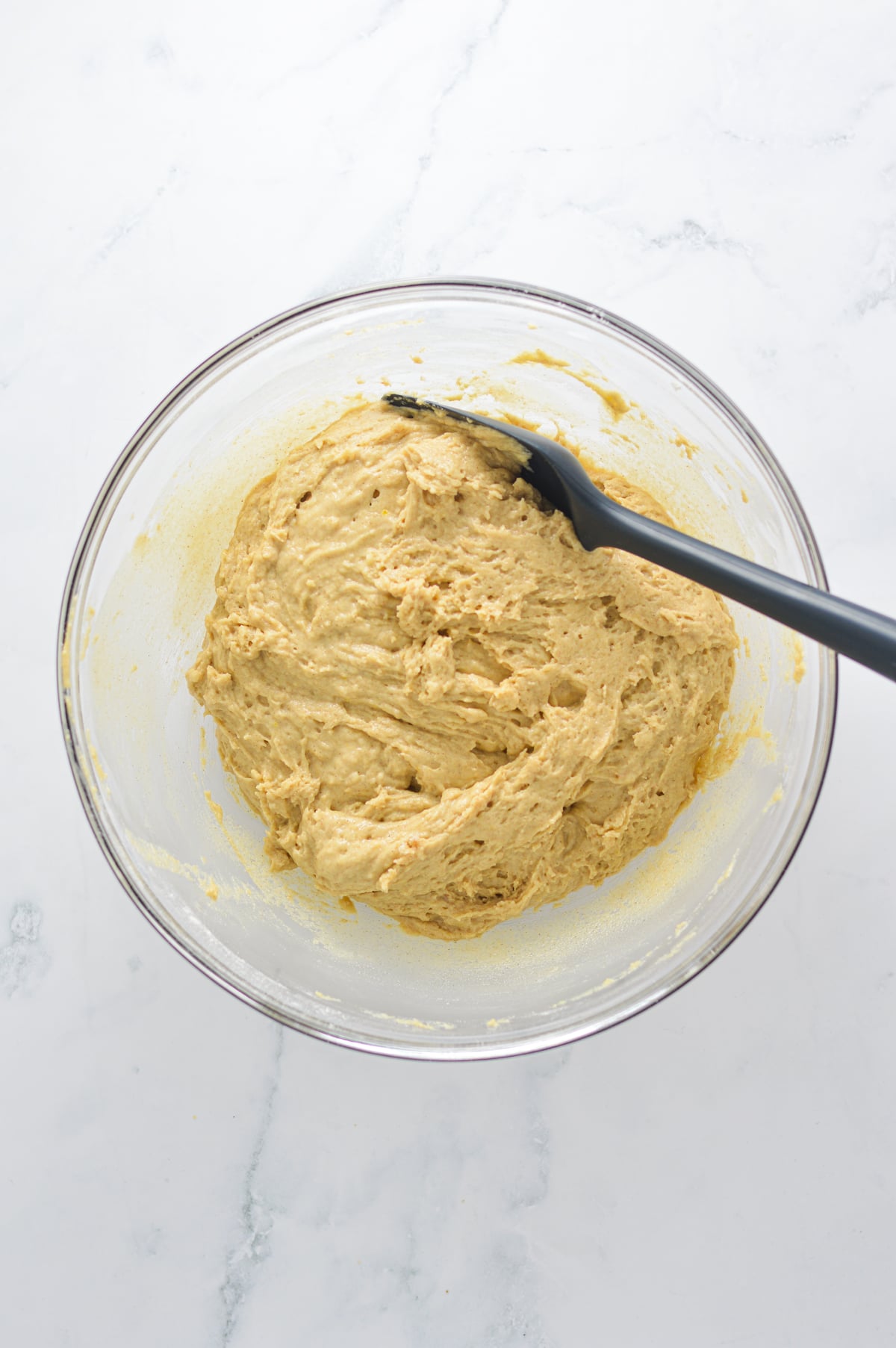 A large bowl with the donut muffins batter in it and a rubber spatula ready to mix the batter.