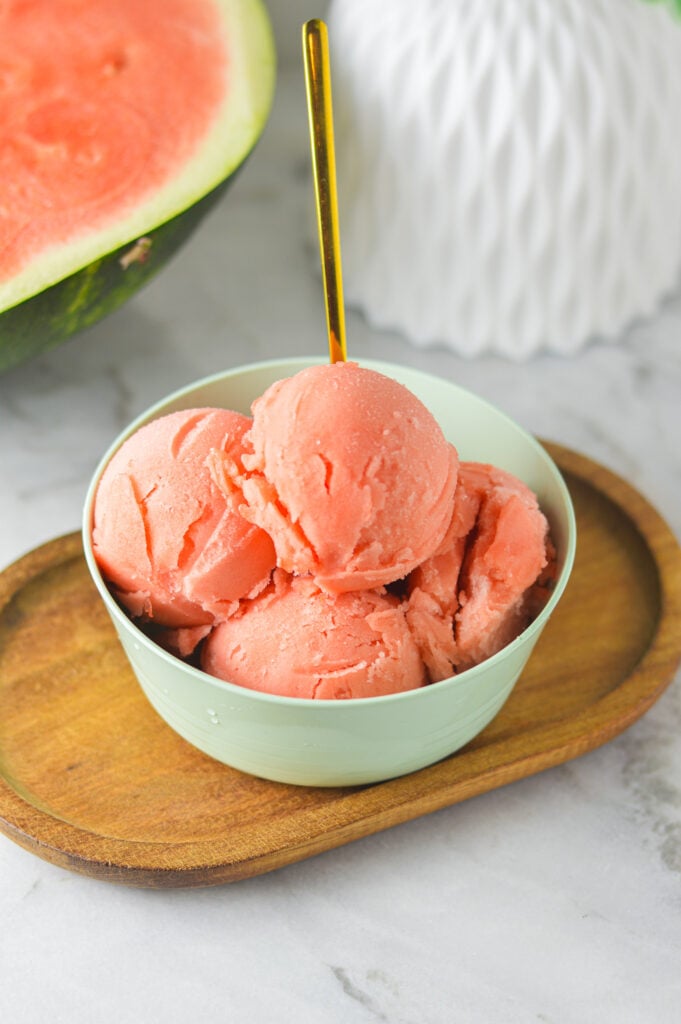 A small bowl with scoops of vibrant Ninja Creami Watermelon Sorbet, a small gold spoon sticking out of the fresh sorbet ready to eat.