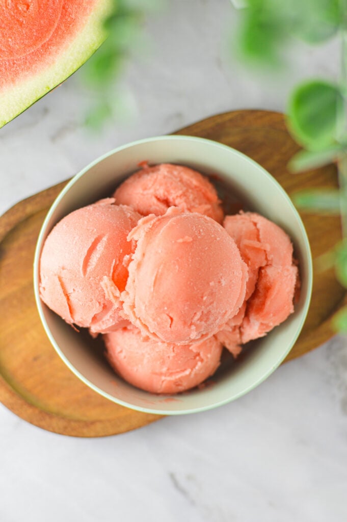 Vibrant pink scoops of Ninja Creami Watermelon Sorbet in a small bowl on a small wooden surface.