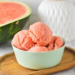 A small bowl filled with fresh Ninja Creami Watermelon Sorbet, with a fresh watermelon wedge in the background.