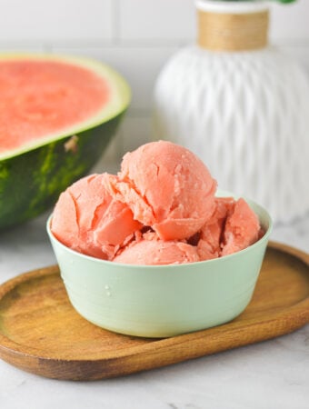 A small bowl filled with fresh Ninja Creami Watermelon Sorbet, with a fresh watermelon wedge in the background.