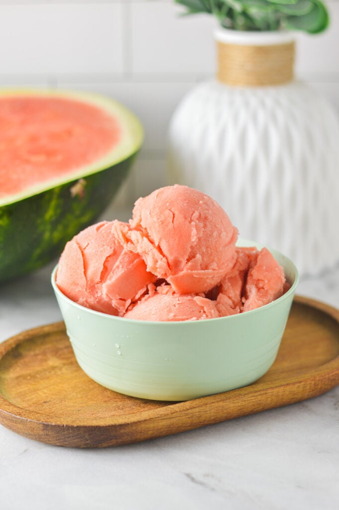 A small bowl filled with fresh Ninja Creami Watermelon Sorbet, with a fresh watermelon wedge in the background.