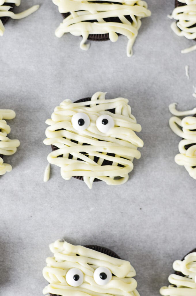 A parchment paper lined baking sheet with Oreo Mummies neatly lined on them.