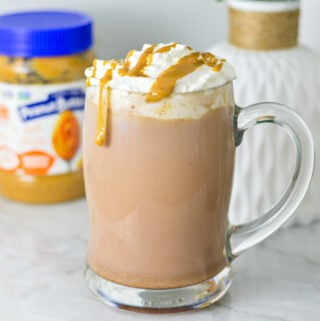 A rich mug of Peanut Butter Hot Chocolate topped with whipped cream, peanut butter drizzle and served in a large glass mug.