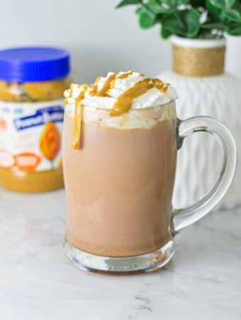 A rich mug of Peanut Butter Hot Chocolate topped with whipped cream, peanut butter drizzle and served in a large glass mug.