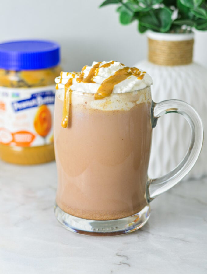 A rich mug of Peanut Butter Hot Chocolate topped with whipped cream, peanut butter drizzle and served in a large glass mug.