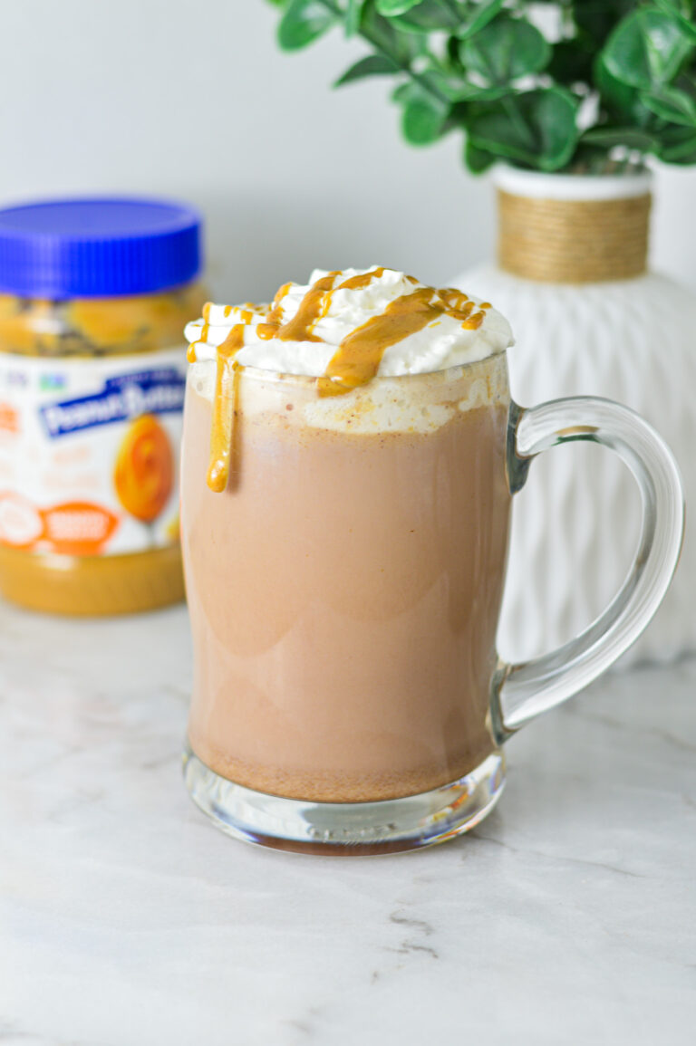 A rich mug of Peanut Butter Hot Chocolate topped with whipped cream, peanut butter drizzle and served in a large glass mug.