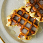 Two golden brown Pillsbury Cinnamon Roll Waffles with a bite taken out of one of them, showing the fluffy texture.