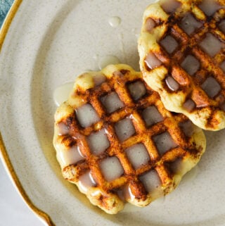 Easy Pillsbury Cinnamon Roll Waffles drizzled with creamy icing on a small ceramic plate.