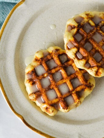Easy Pillsbury Cinnamon Roll Waffles drizzled with creamy icing on a small ceramic plate.