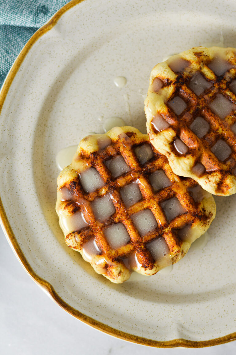 Easy Pillsbury Cinnamon Roll Waffles drizzled with creamy icing on a small ceramic plate.