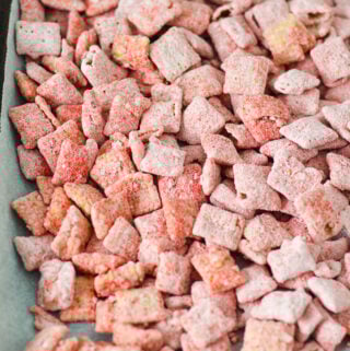A parchment paper lined baking sheet covered in Strawberry Puppy Chow, with each piece of chex cereal covered in bright red strawberry dusting.