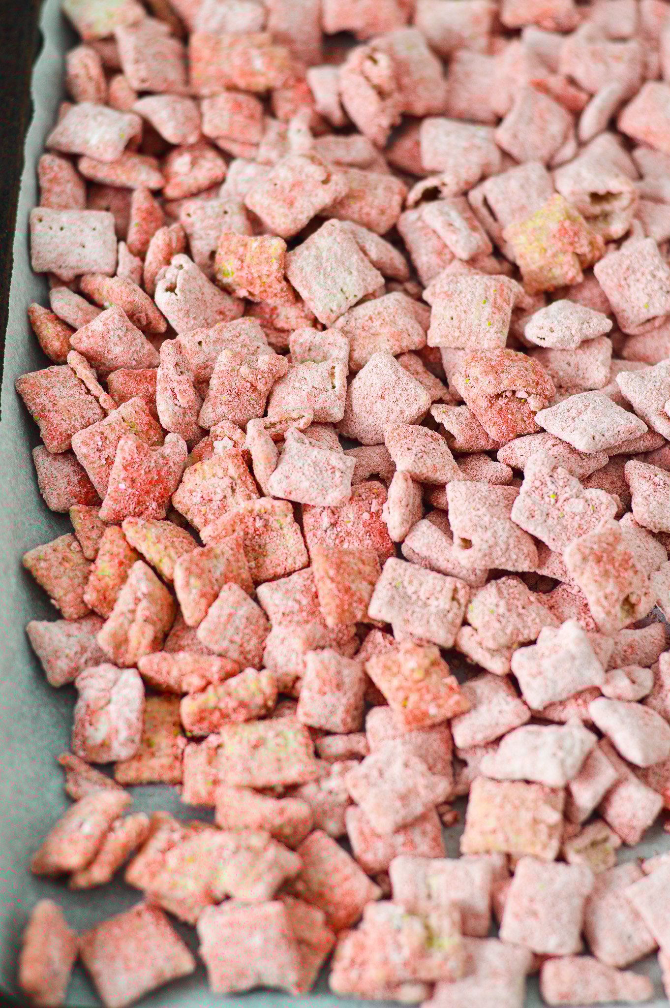 A parchment paper lined baking sheet covered in Strawberry Puppy Chow, with each piece of chex cereal covered in bright red strawberry dusting.