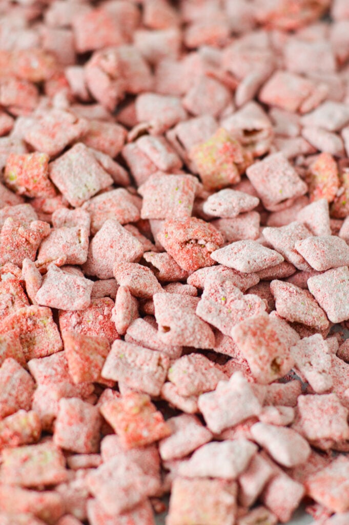 A parchment paper lined baking tray full of vibrant red Strawberry Puppy Chow.