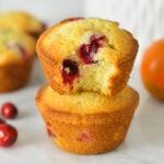 A stack of Cranberry Orange Muffins with a bite taken out of the top muffin, showing the soft and fluffy texture.