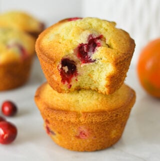 A stack of Cranberry Orange Muffins with a bite taken out of the top muffin, showing the soft and fluffy texture.