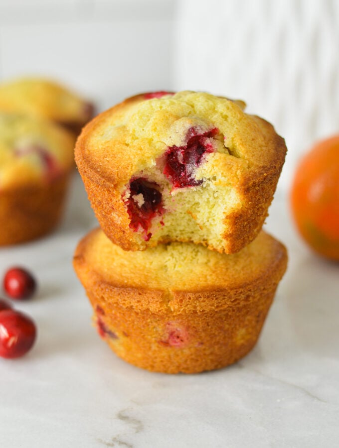 A stack of Cranberry Orange Muffins with a bite taken out of the top muffin, showing the soft and fluffy texture.