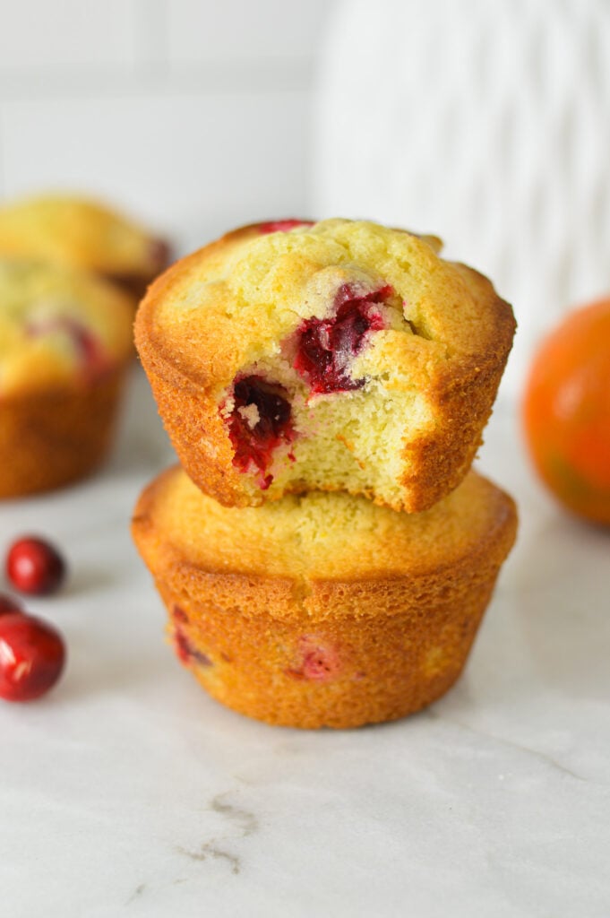 A stack of Cranberry Orange Muffins with a bite taken out of the top muffin, showing the soft and fluffy texture.