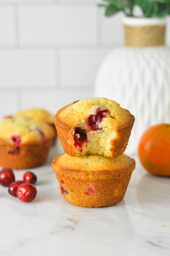 Some Cranberry Orange Muffins on a granite surface with some fresh cranberries and oranges in the background.