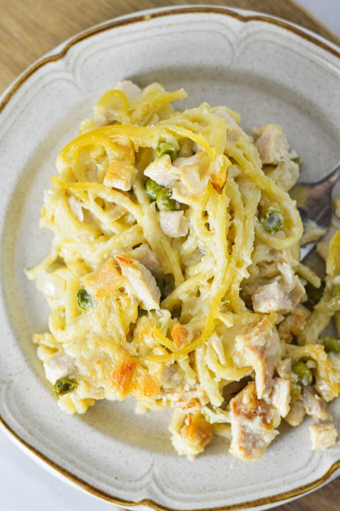 A fork inserted into a plate full of creamy Leftover Turkey Tetrazzini, with turkey chunks, peas and spaghetti mixed into this delicious dish.