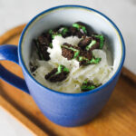 A coffee cup full of Mint Oreo Hot Chocolate, topped with whipped cream and mint Oreo chunks on top.