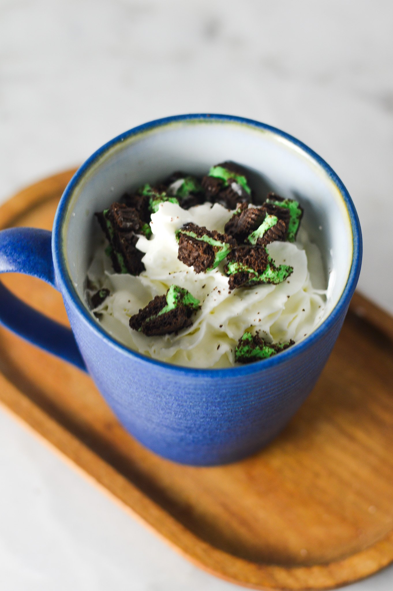 A coffee cup full of Mint Oreo Hot Chocolate, topped with whipped cream and mint Oreo chunks on top.