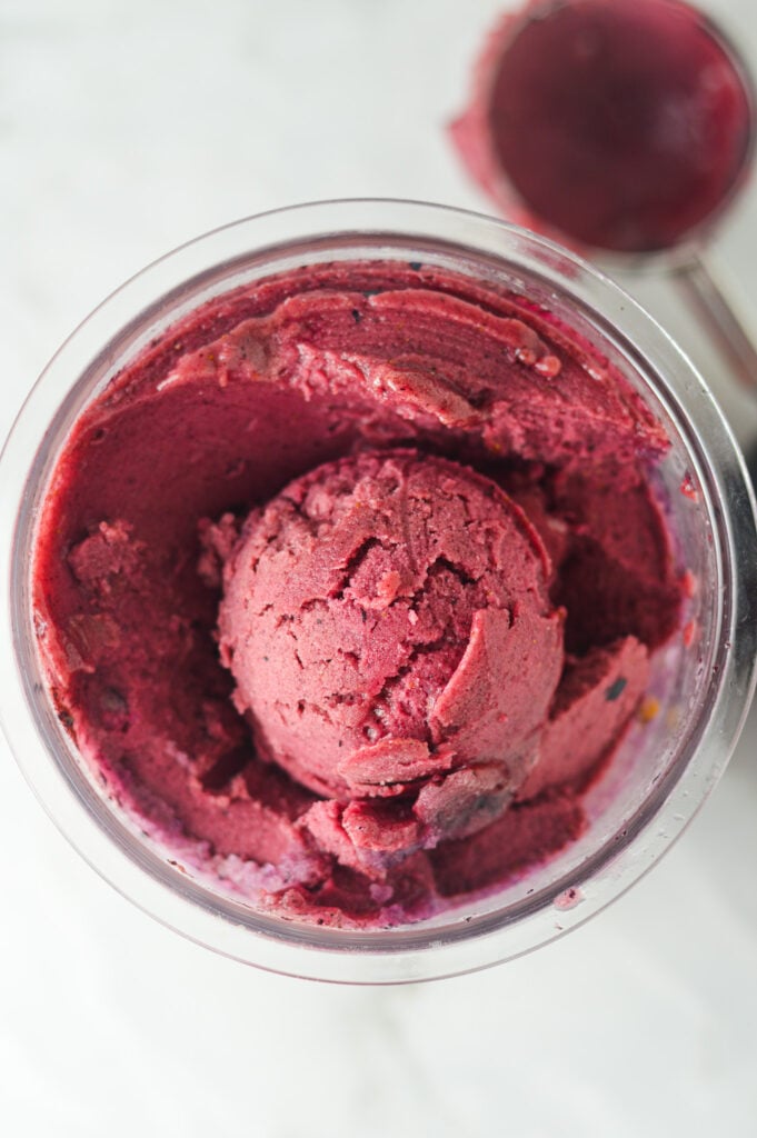 A Ninja Creami pint full of Ninja Creami Blueberry Watermelon Sorbet, with a scoop on top clearly showing the creamy texture.