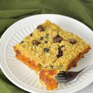 A square piece of Chocolate Chip Baked Oatmeal on a white plate with a fork taking out a bite from the warm oatmeal.