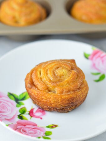 Golden brown Cinnamon Sugar Crescent Roll Muffins on a small plate, with a muffin tin filled with freshly baked muffins.