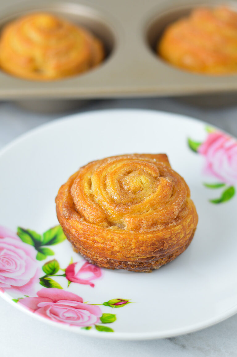 Golden brown Cinnamon Sugar Crescent Roll Muffins on a small plate, with a muffin tin filled with freshly baked muffins.