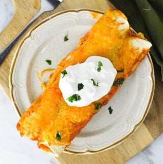 A plate with some Easy Leftover Turkey Enchiladas topped with melted Mexican blend cheese, sour cream and chopped cilantro.