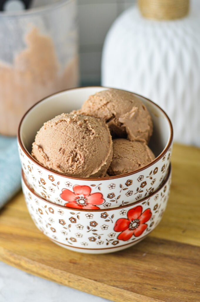 A small bowl filled with Ninja Creami Chocolate Ice Cream with a Ninja Creami Pint container in the background.