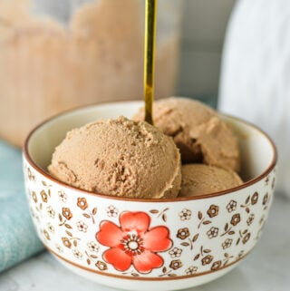 A gold spoon coming out of a bowl full of Ninja Creami Chocolate Ice Cream, with a Ninja Creami container in the background.