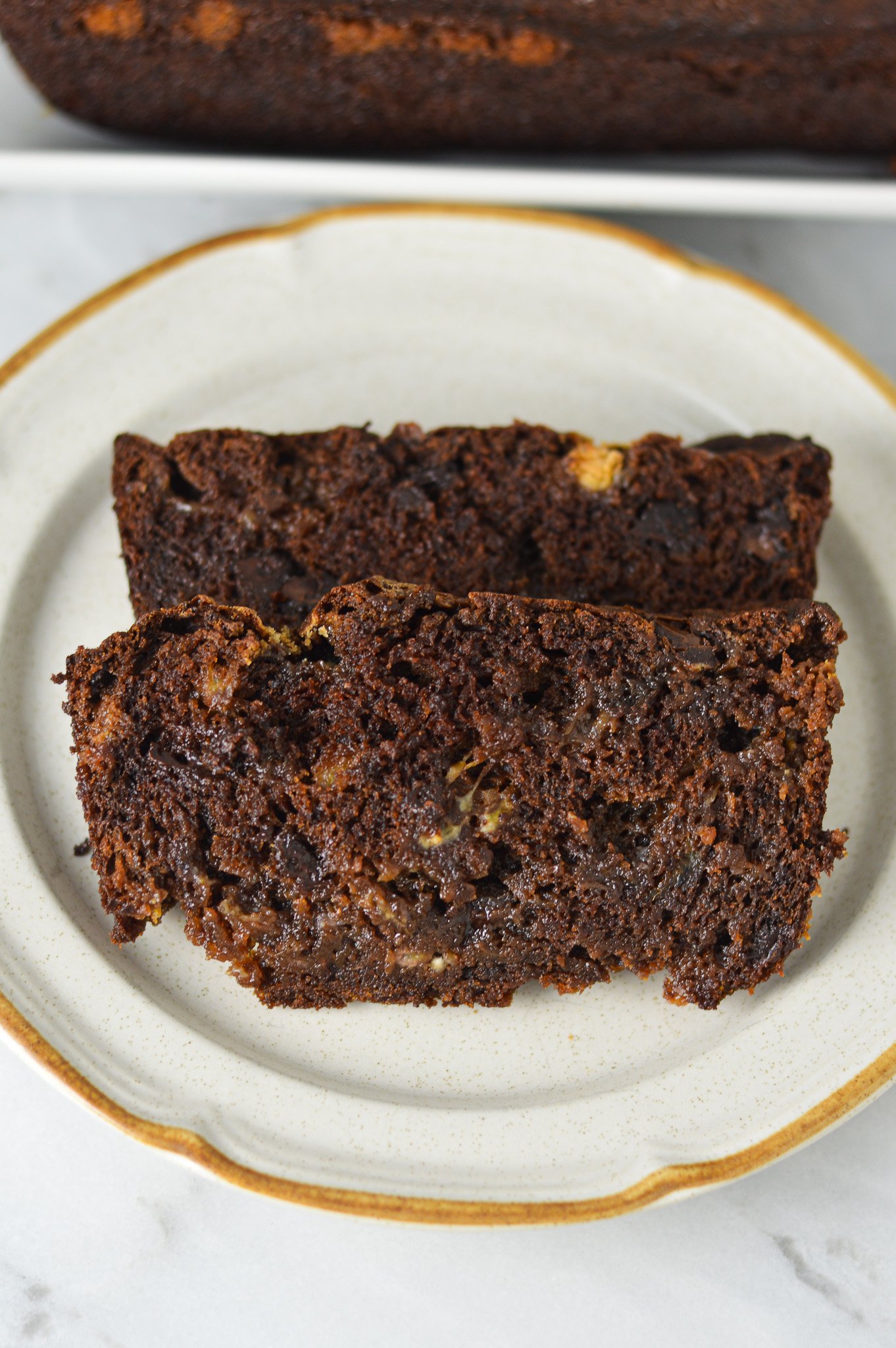 Two slices of homemade Triple Chocolate Banana Bread, with semi-sweet and white chocolate chips studded in the rich chocolate bread.