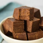 Squares of 3 Ingredient Chocolate Peanut Butter Fudge arranged in a shallow bowl with a bite taken out of the top piece of fudge, showing its rich texture.
