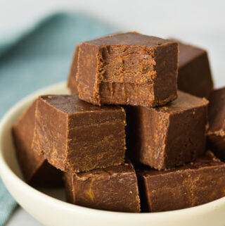 Squares of 3 Ingredient Chocolate Peanut Butter Fudge arranged in a shallow bowl with a bite taken out of the top piece of fudge, showing its rich texture.
