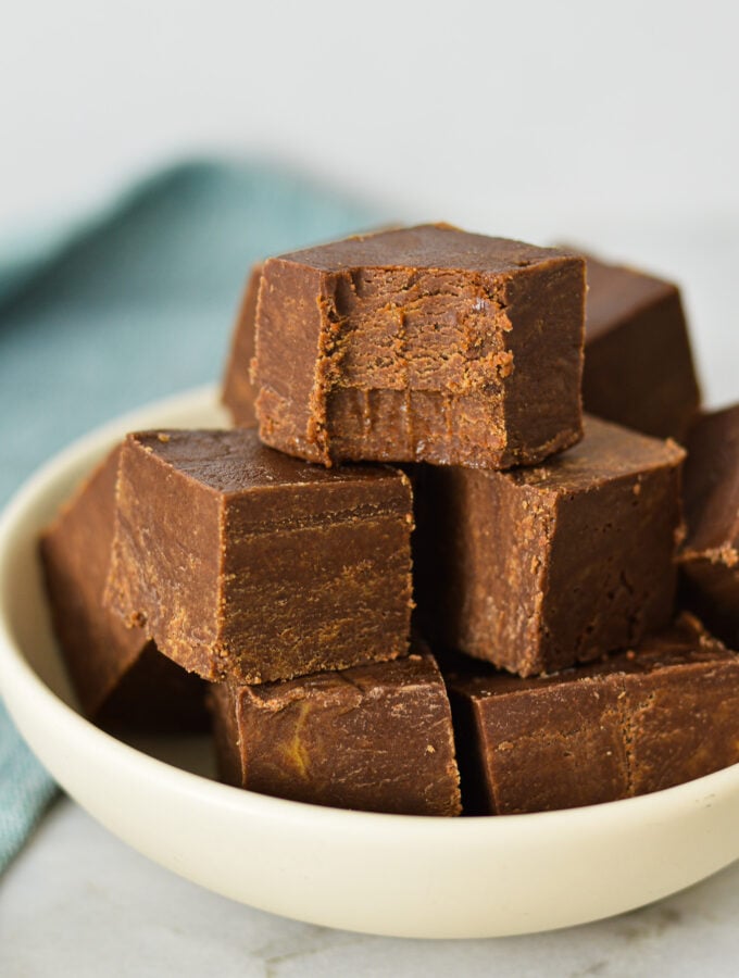 Squares of 3 Ingredient Chocolate Peanut Butter Fudge arranged in a shallow bowl with a bite taken out of the top piece of fudge, showing its rich texture.