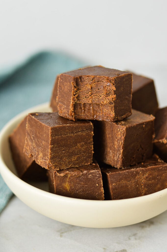 Squares of 3 Ingredient Chocolate Peanut Butter Fudge arranged in a shallow bowl with a bite taken out of the top piece of fudge, showing its rich texture.