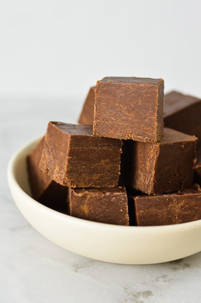 Small squares of 3 Ingredient Chocolate Peanut Butter Fudge arranged on a white bowl, showing the glossy texture and creamy layers.