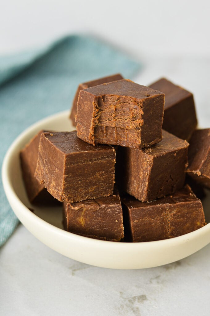 Homemade Chocolate Peanut Butter Fudge on a small plate with a bite taken out of the top fudge square showing its smooth texture.