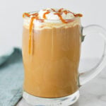 A steaming cup of Caramel Mocha topped with whipped cream and caramel sauce, served in a glass mug on a granite surface.