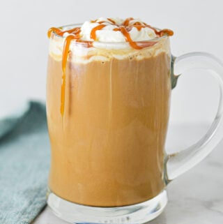 A steaming cup of Caramel Mocha topped with whipped cream and caramel sauce, served in a glass mug on a granite surface.