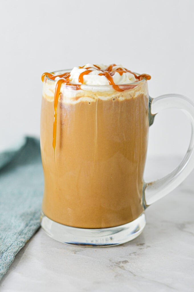 A steaming cup of Caramel Mocha topped with whipped cream and caramel sauce, served in a glass mug on a granite surface.