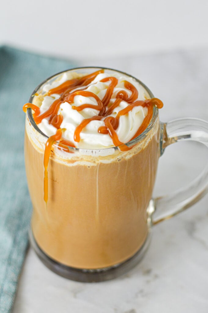 A glass mug filled with Caramel Mocha and topped with whipped cream with caramel sauce drizzled on top.