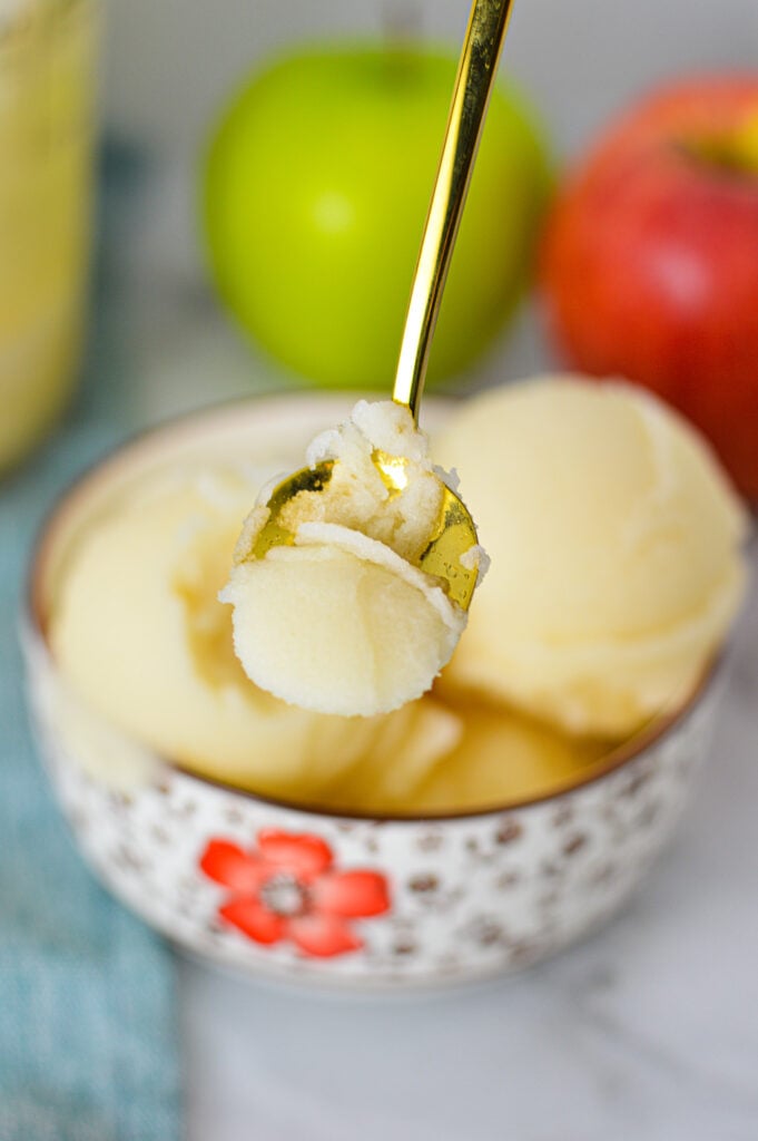 A gold spoon taking a scoop of Ninja Creami Apple Italian Ice from a small bowl filled with the refreshing treat.