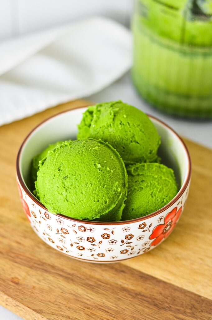 A vibrant green bowl of Ninja Creami Matcha Ice Cream, with a Ninja Creami Pint container filled with ice cream in the background.