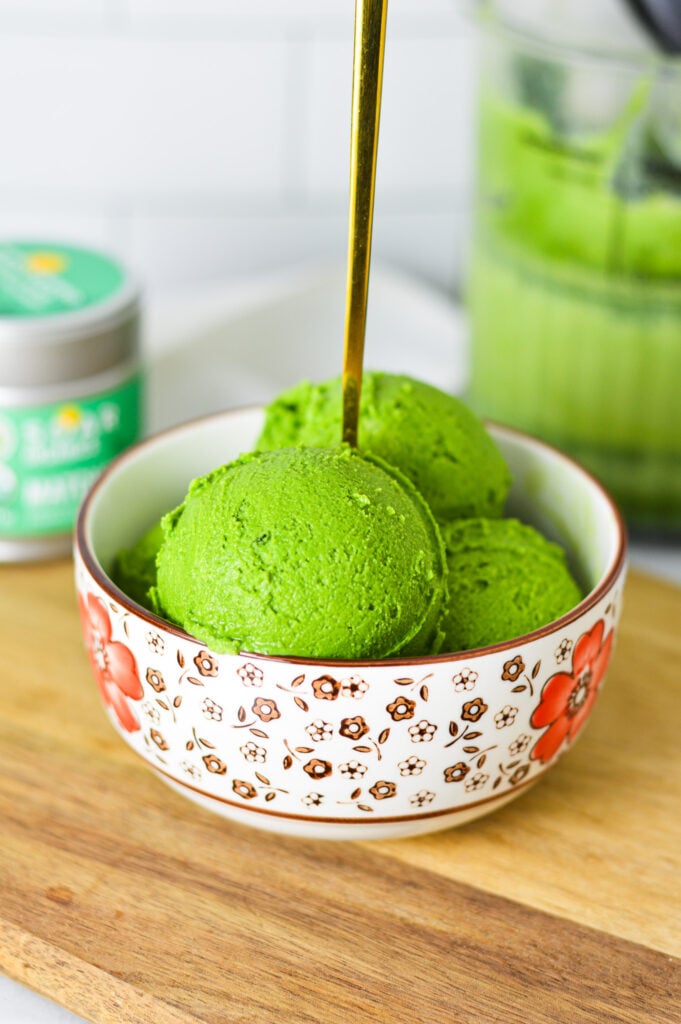 A gold spoon in a bowl full of Ninja Creami Matcha Ice Cream, with some matcha powder in the background.