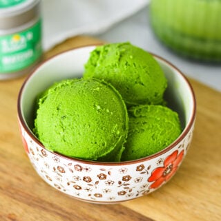 A small bowl filled with bright green Ninja Creami Matcha Ice Cream, with green tea powder in the background.