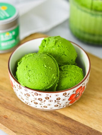 A small bowl filled with bright green Ninja Creami Matcha Ice Cream, with green tea powder in the background.